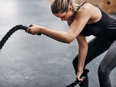 Fit young woman swinging ropes during a gym workout Fit young blonde woman in sportswear working out with ropes during an exercise session in a gym