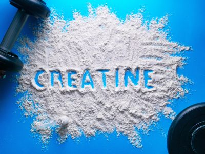 Scattered powder with the word creatine written on it on a blue background. Scattered powder with the word creatine written on it on a blue background.